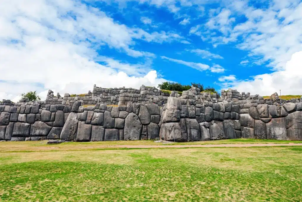 Sacsayhuaman ramparts with massive interlocking stones and open green field in Cusco, Peru