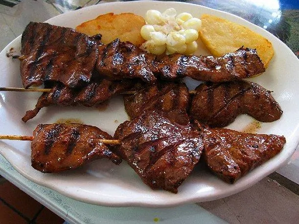 Los 12 Platos que Debes Probar en Perú y Dónde Encontrarlos (Guía 2026) 5 Peruvian anticuchos with corn and potatoes