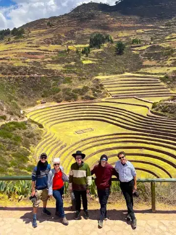 Valle Sagrado vs Cusco: ¿Cuál es mejor para tu viaje a Perú? 1 Visitors standing in front of the circular agricultural terraces of Moray in the Sacred Valley of Peru.
